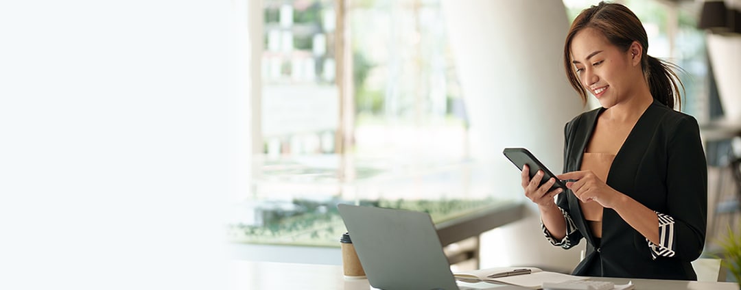 A business owner at a desk checking her bank account on her smartphone
